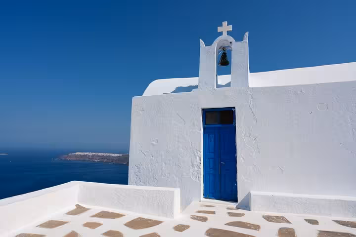 Whitewashed Santorini chapel with blue door and sea view, stop on private SUV hidden gems tour