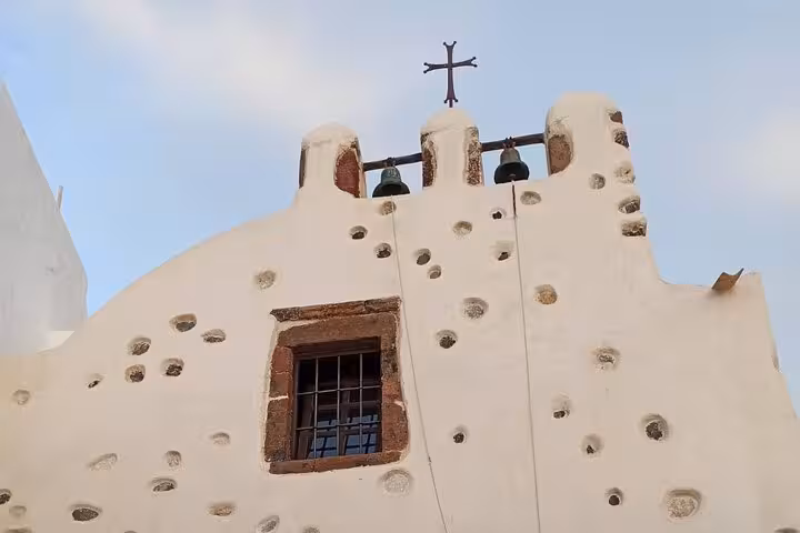 Santorini church belfry with cross and bells on whitewashed facade, seen on a private 3-day island tour with transfer