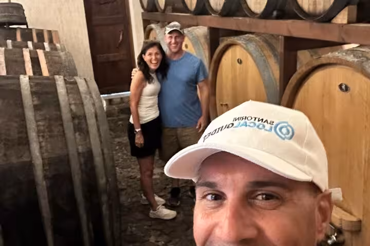 Couple in a Santorini winery cellar with oak barrels on a private wine tasting tour featuring tastings and lunch