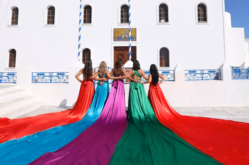 Group flying dress photoshoot in Santorini at a white church, colorful gowns with long trains flowing