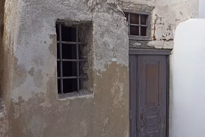 Rustic Santorini house facade with barred window and wooden door, part of a private 3-day tour with transfers included