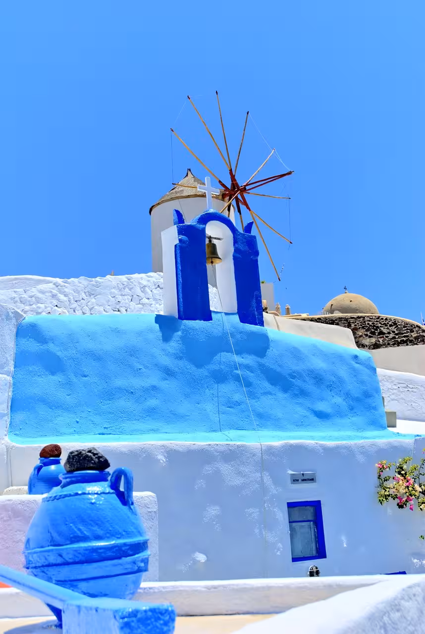 Blue and white Santorini chapel with bell and windmill in Oia, iconic photo stop on cruise shore tour