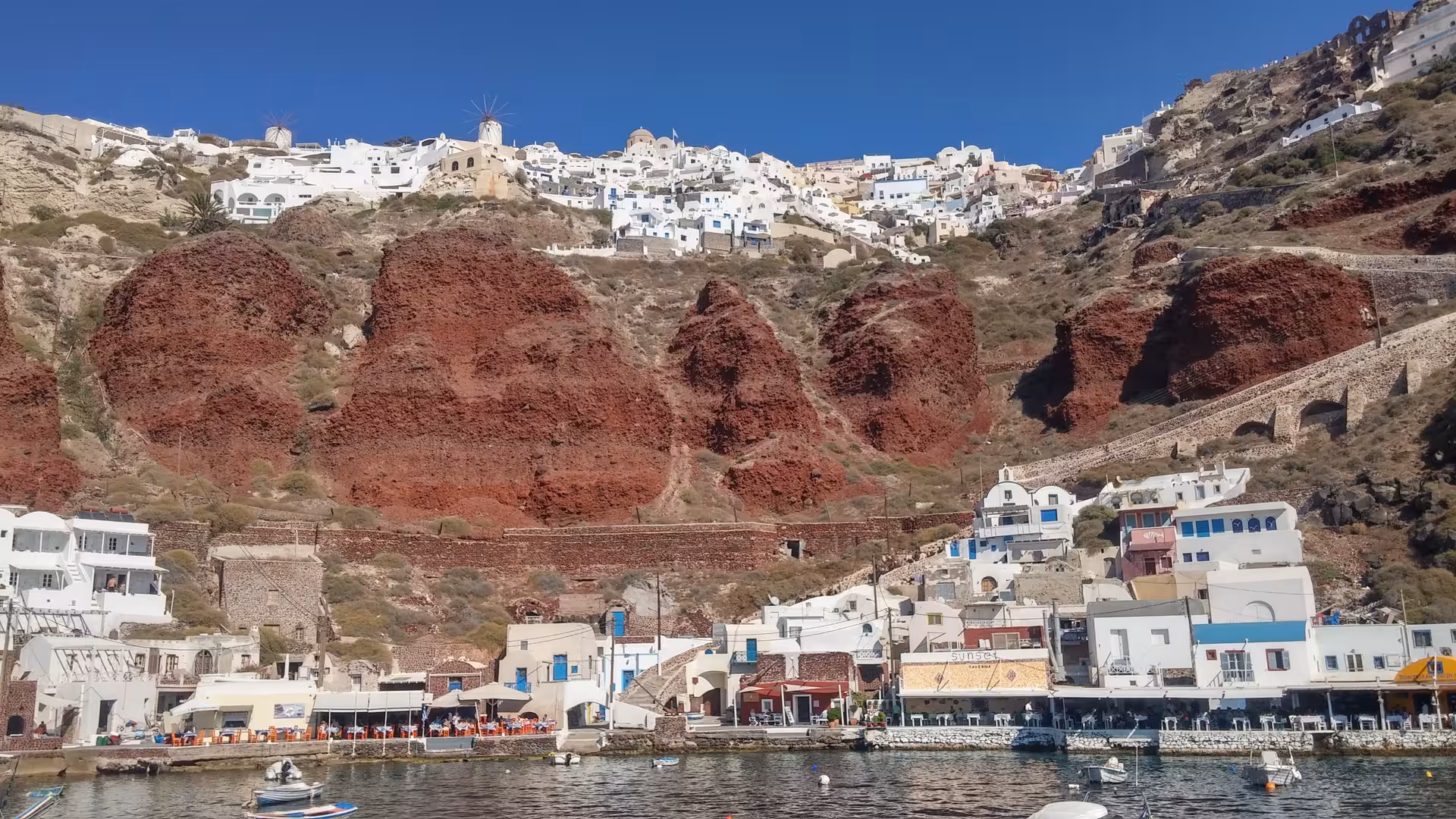 Santorini cruise shore excursion view of whitewashed Oia village above red cliffs and harbor boats