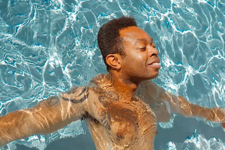 Man floating in a crystal-clear private pool in Santorini, luxury caldera-view day and sunset escape