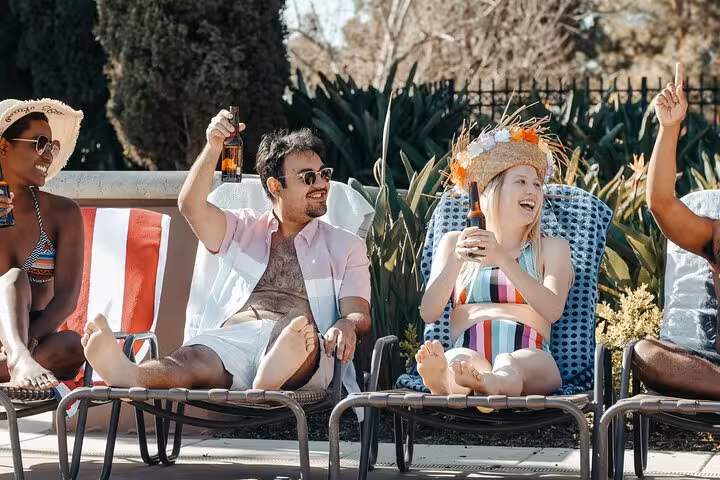 Group lounging poolside with drinks, enjoying Santorini private pool day with caldera and sunset views