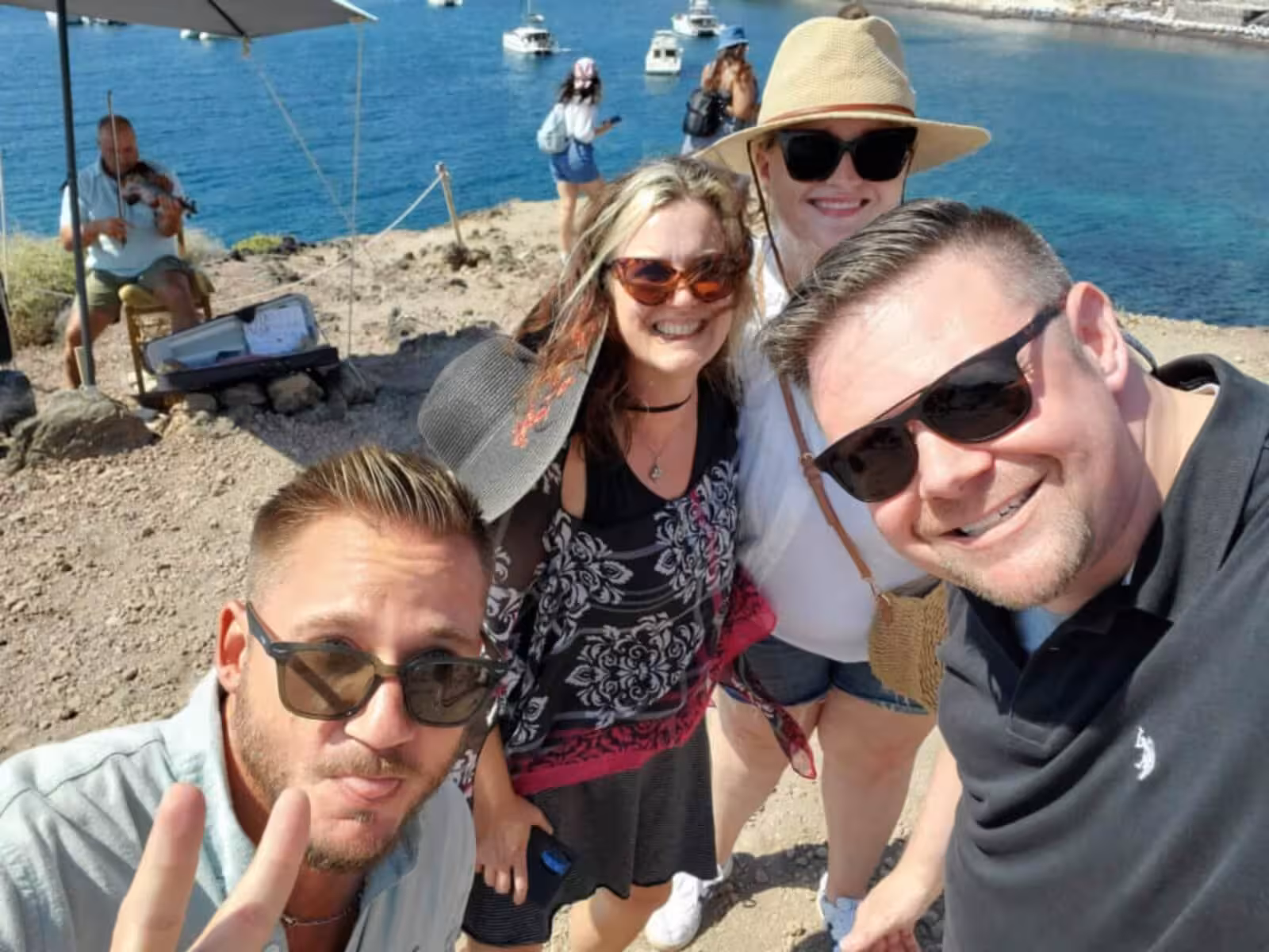Friends selfie at Santorini caldera viewpoint on private tour, Aegean sea and boats behind, sunny day