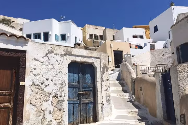 Santorini private tour stop at whitewashed cave houses and stone steps, classic Cycladic architecture under blue sky
