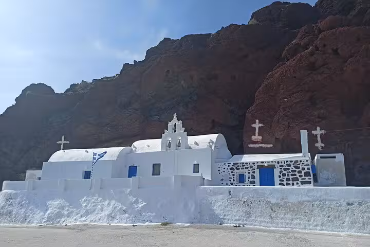 Whitewashed seaside chapel on Santorini beneath volcanic cliffs, private 3-day island tour with transfers included