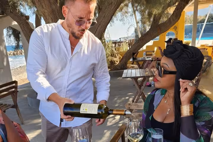 Sommelier pouring Santorini wine at a seaside taverna, part of a tailored private island tour experience