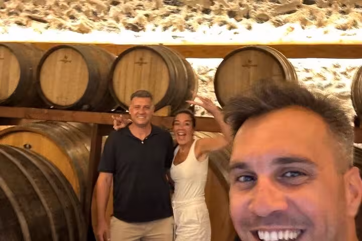 Guests posing in a Santorini winery barrel cellar during a private wine tasting tour with lunch and cellar visit