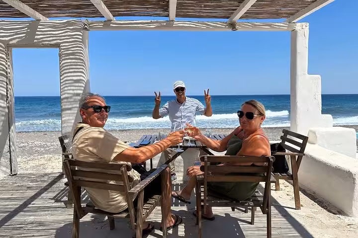 Guests toast with Santorini wine at a seaside taverna stop on a private wine tasting tour with lunch
