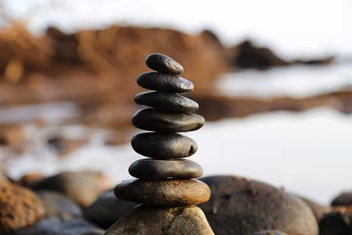 Stacked zen stones on rocky shore, calming Santorini Serenity Yoga mindfulness moment by the Aegean