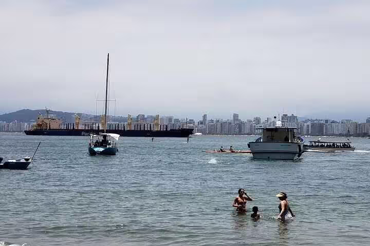 Relaxing beach scene in Santos with people swimming and boats sailing against a city skyline backdrop.