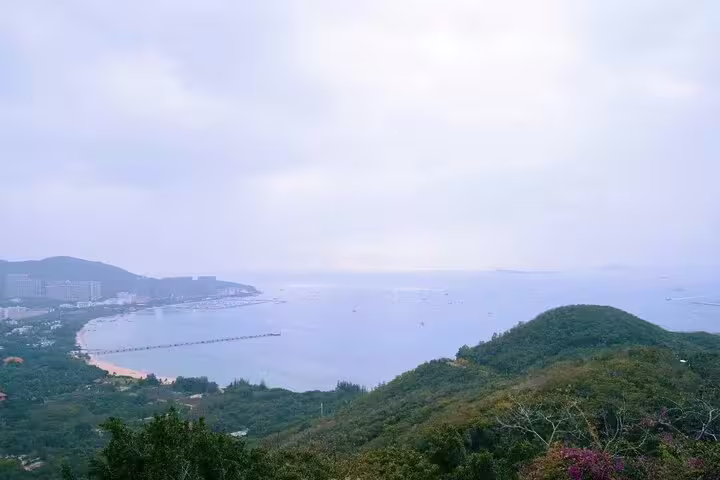 Scenic view of the coastline and lush hills in Sanya, highlighting the natural beauty of the Luhuitou area on a clear day.