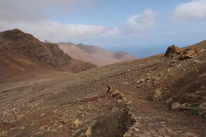 Scenic landscape of São Nicolau's Juncalinho Trail with mountain vistas and rocky paths under a bright sky.