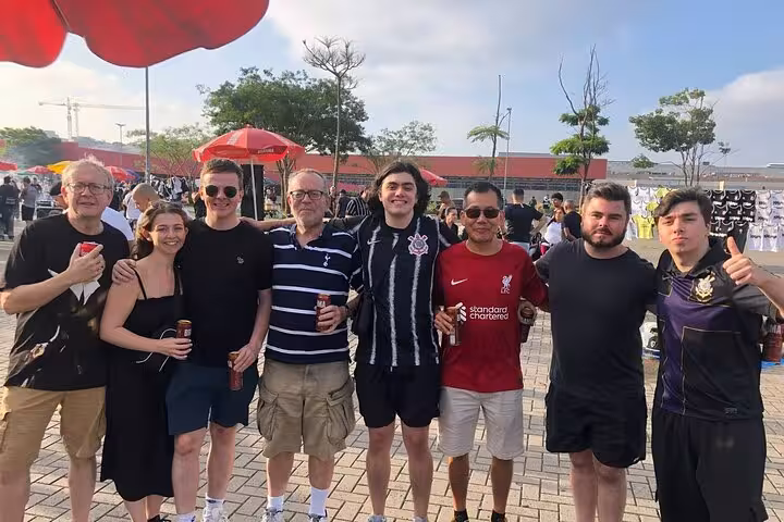 Tour group meeting locals outside São Paulo stadium before pickup soccer game, wearing team jerseys and smiling
