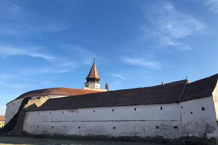 Medieval Saxon fortification wall with defensive tower and pointed spire under blue sky in Transylvania