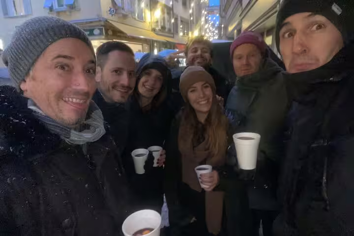 Friends enjoying warm drinks on a Schaffhausen scavenger hunt, exploring old town sights at dusk in winter