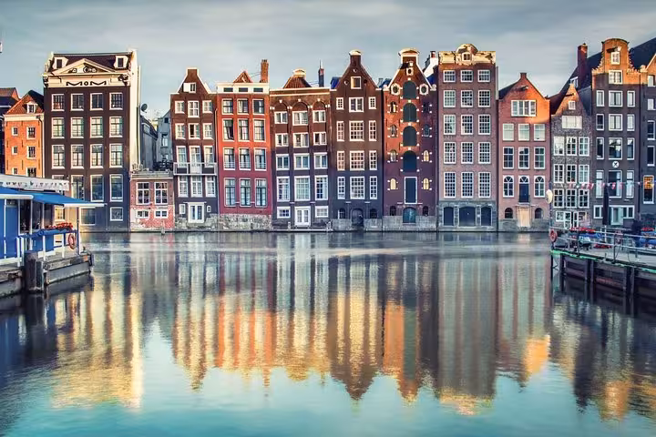 Amsterdam canal houses reflected on water, scenic city destination after Schiphol Airport to Amsterdam private transfer