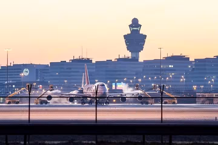 Schiphol Airport runway at dusk with aircraft and control tower, meeting point for private transfer to Antwerp