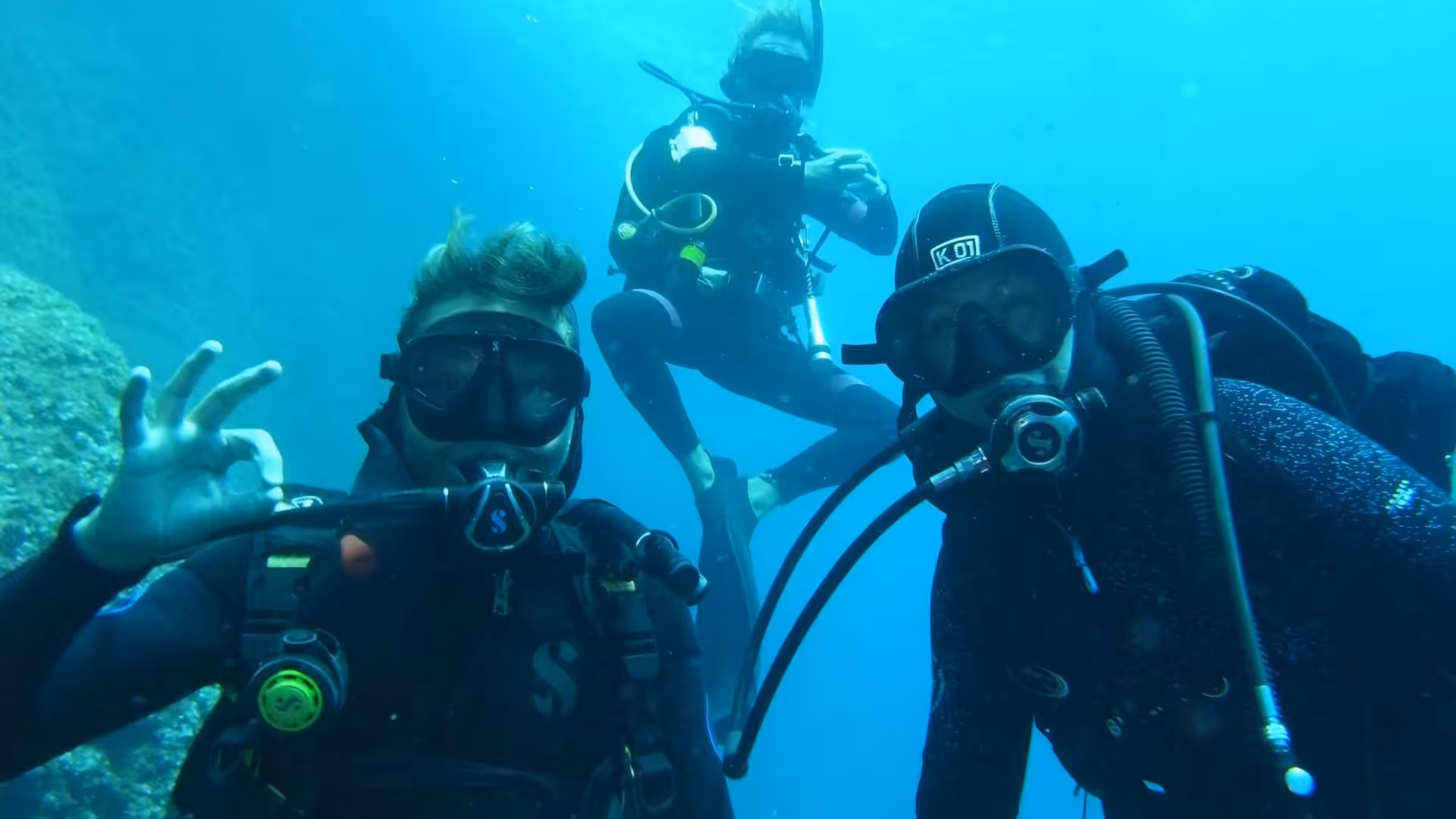 Three scuba divers signal OK while exploring the crystal-clear waters of Argentiera, Sassari on an underwater adventure.
