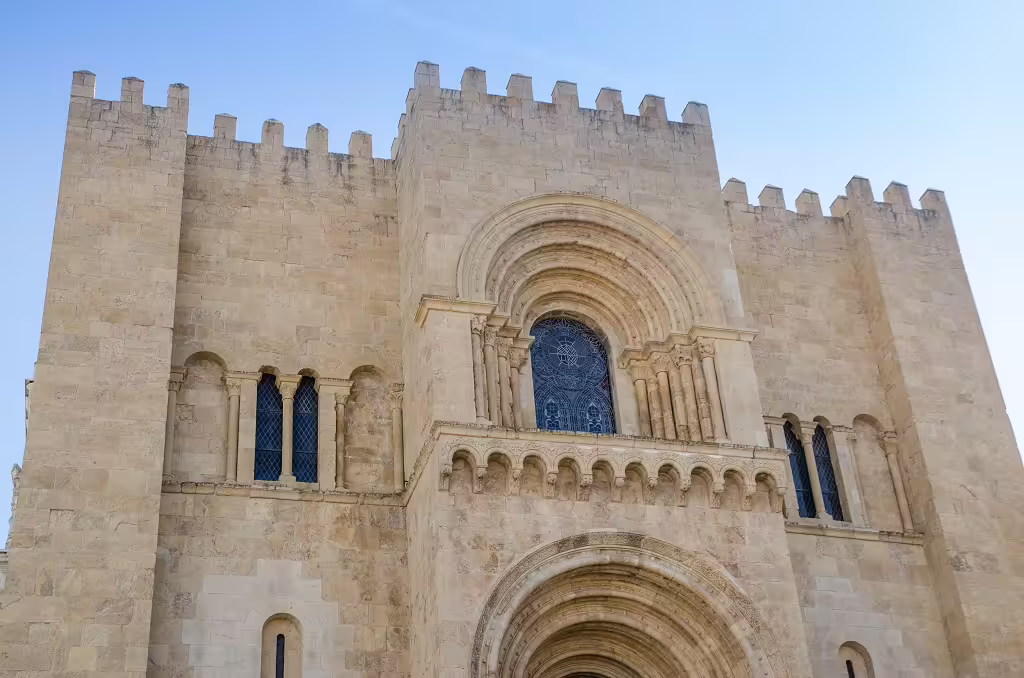 Exterior view of the historic Sé Velha Cathedral in Coimbra, Portugal, showcasing Romanesque architecture under a clear blue sky.