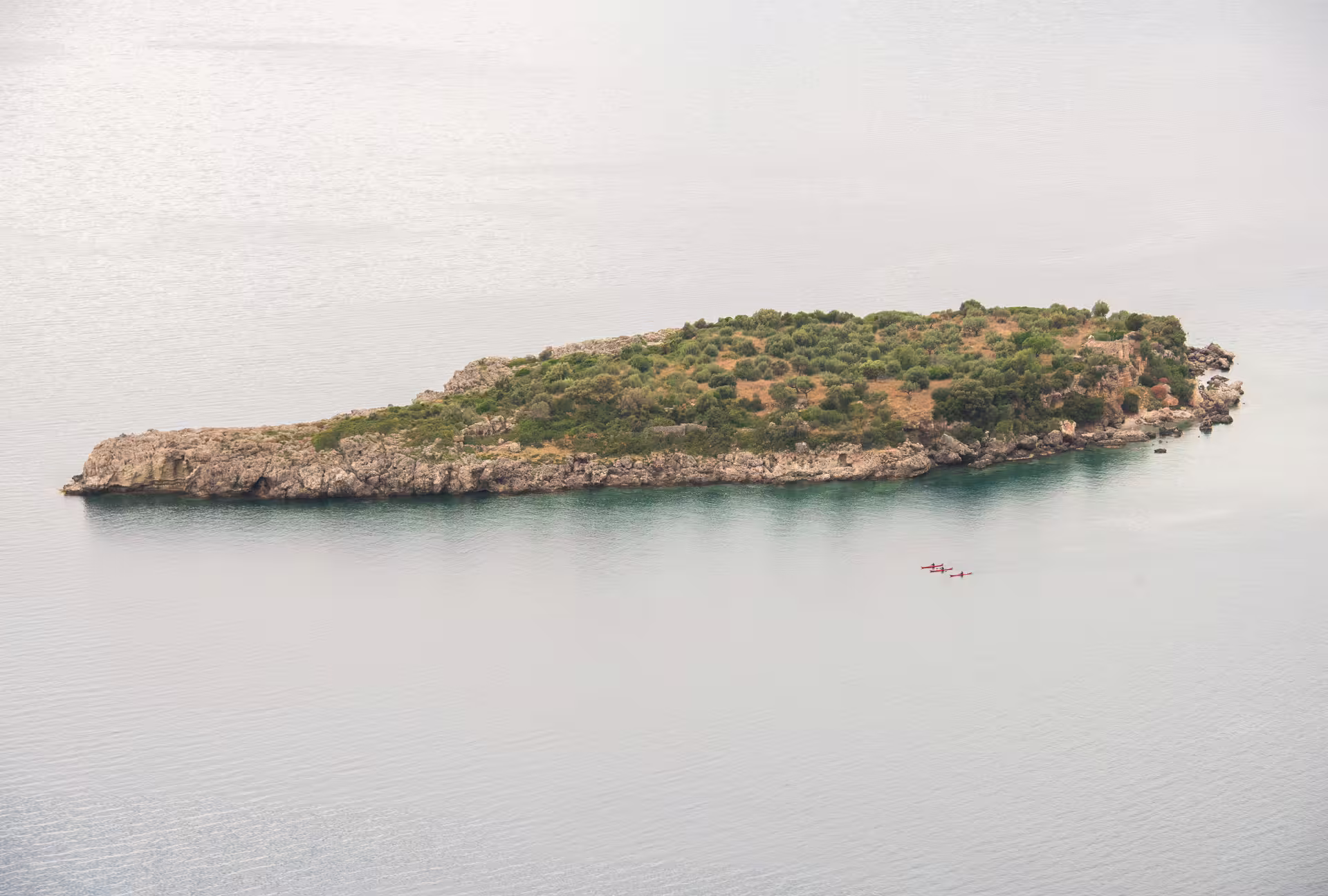 Aerial view of kayaks paddling past a rocky islet off Kardamyli and Stoupa on a sea kayaking adventure