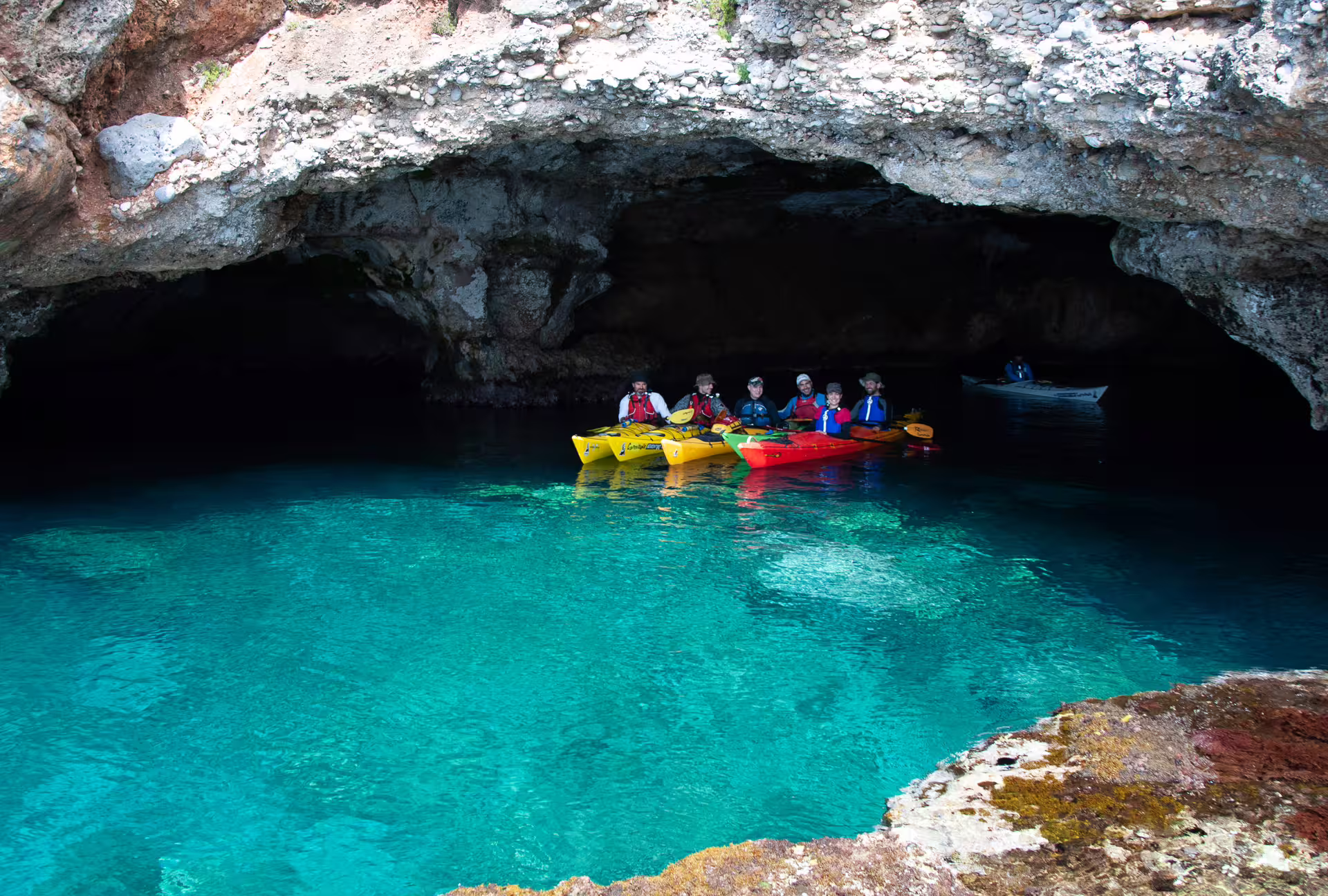 Sea kayakers exploring a sea cave on the Kardamyli and Stoupa tour, floating on vivid blue water in Mani