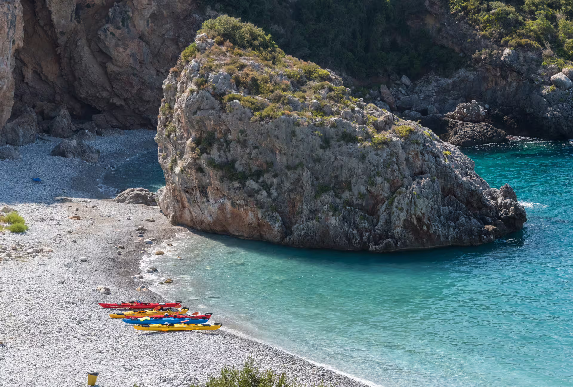 Colorful sea kayaks on a pebble beach cove near Kardamyli and Stoupa, with turquoise Mani waters