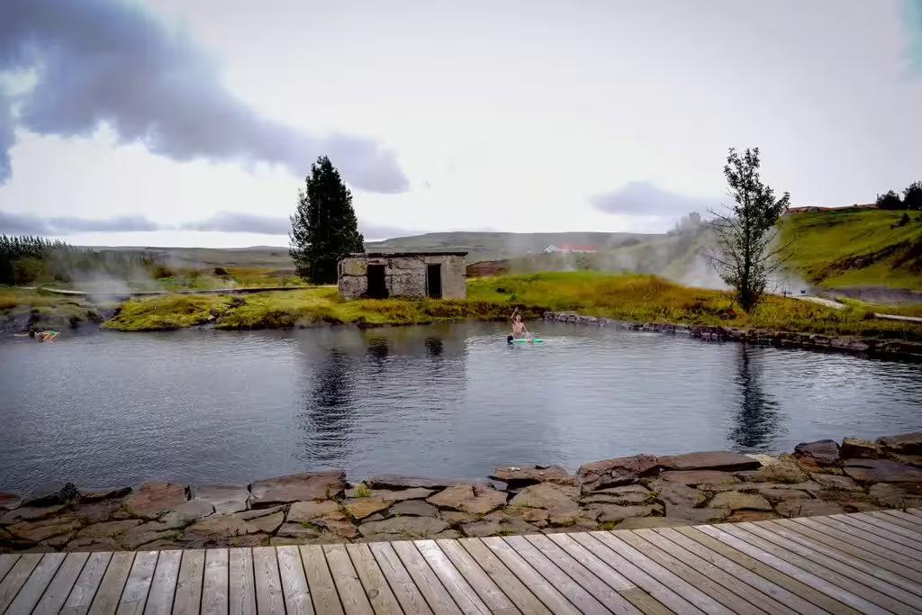Steaming Secret Lagoon geothermal pool with stone ruins and wooden deck in Iceland