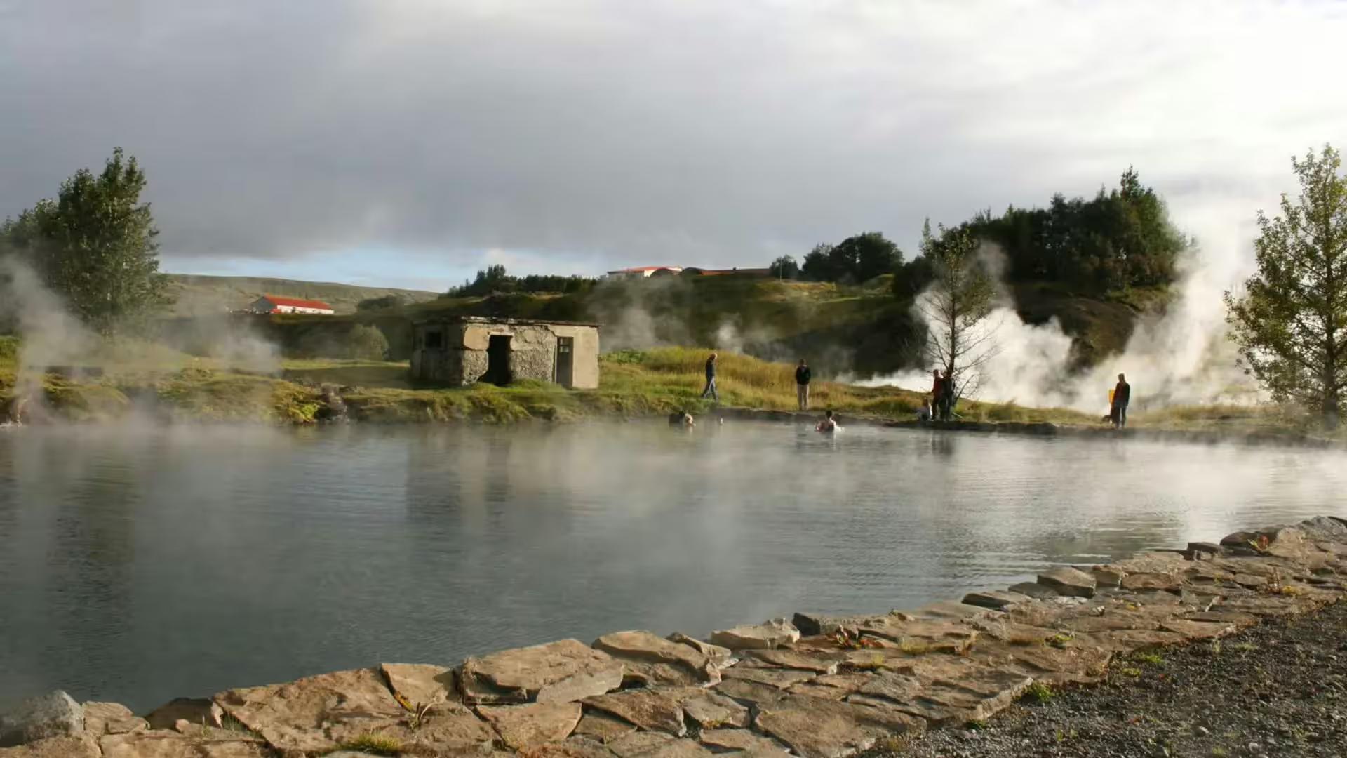 Steaming geothermal Secret Lagoon hot spring pool with visitors and stone building in Iceland's Golden Circle