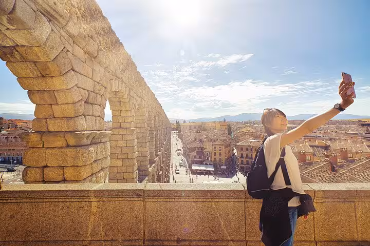 Visitor takes a selfie at the historic Roman aqueduct in Segovia on a sunny day during a guided tour from Madrid.