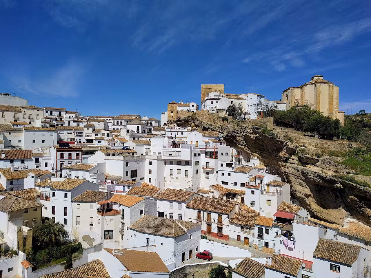 Scenic view of Setenil de las Bodegas village with whitewashed houses built into cliffs under a clear blue sky.