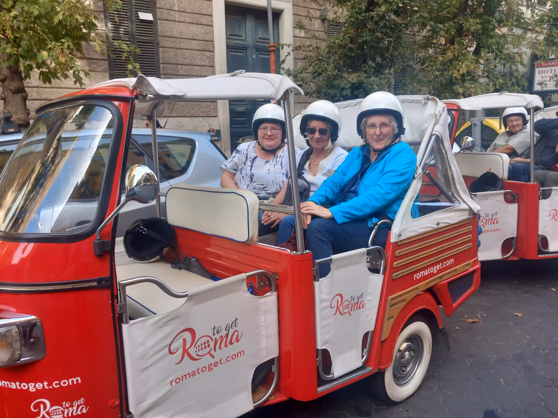 Smiling group of tourists in red tuk-tuks ready for the 7 churches tour during Jubilee 2025 in Rome.