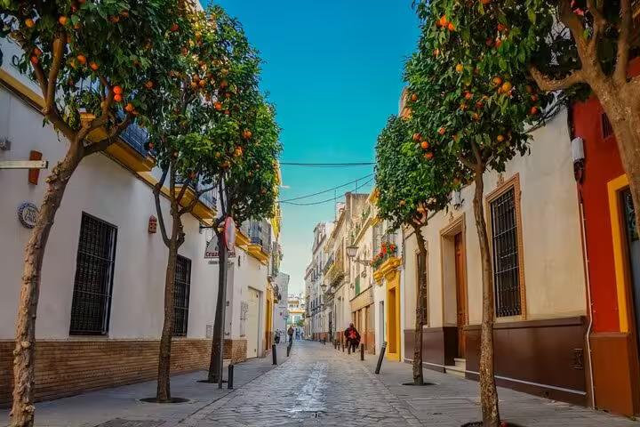 Charming cobblestone street lined with orange trees and colorful buildings in Seville's historic neighborhood