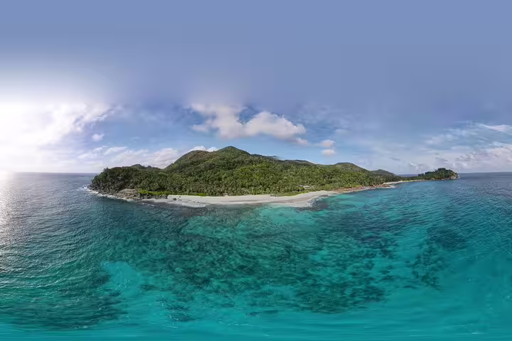 Panoramic view of lush green island and clear blue seas at Anse Major, highlighting snorkeling tour beauty.