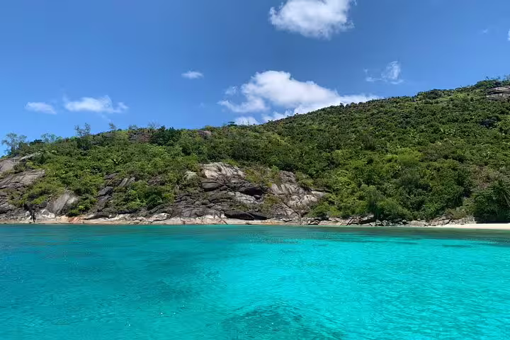 Pristine beach at Anse Major with vibrant blue waters and verdant hillside, perfect for a snorkeling and BBQ tour.