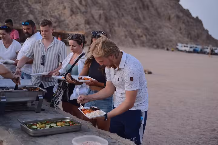 Travelers serving BBQ buffet in Sinai Desert camp on Sharm El Sheikh ATV quad tour with stargazing experience