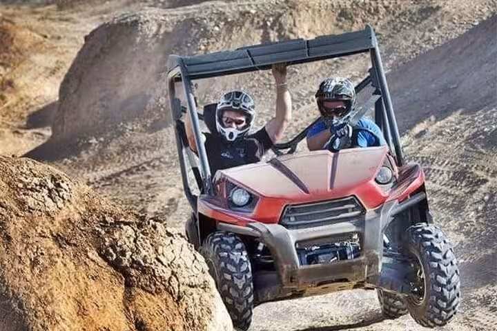 Two riders in helmets driving a dune buggy through rocky terrain near Sharm El-Sheikh on a desert safari tour