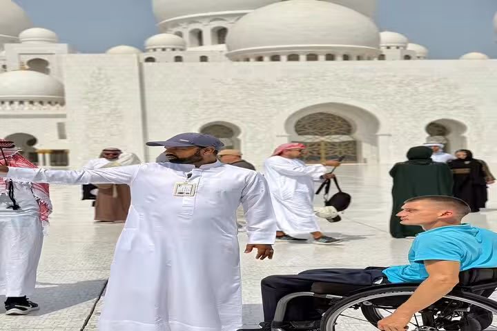 Tour guide assisting wheelchair guest at Sheikh Zayed Grand Mosque courtyard, Abu Dhabi mosque visit