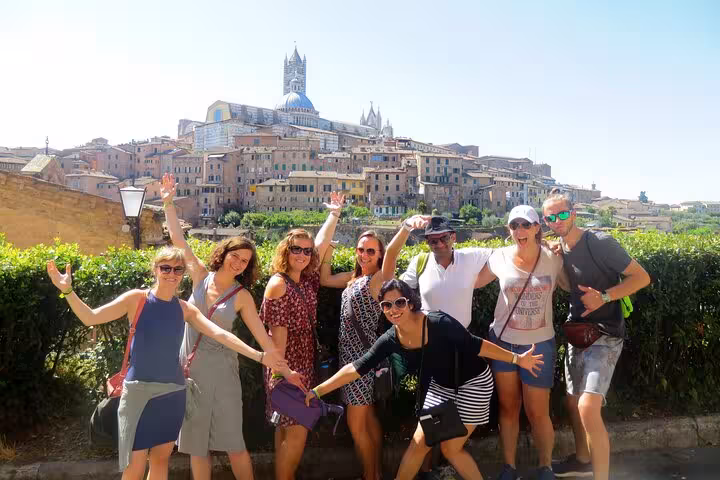 Happy tourists posing with Siena's historic skyline in the background on a Tuscany wine tasting tour.