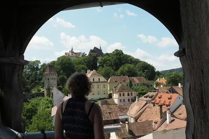Traveler viewing Sighisoara medieval citadel rooftops and hilltop church through stone archway, Transylvania
