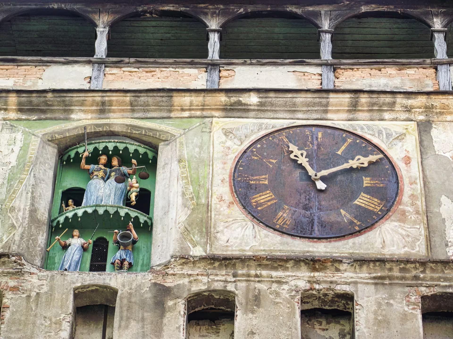 Close-up of Sighisoara Clock Tower facade with ornate figurines and Roman numeral clock face in Transylvania