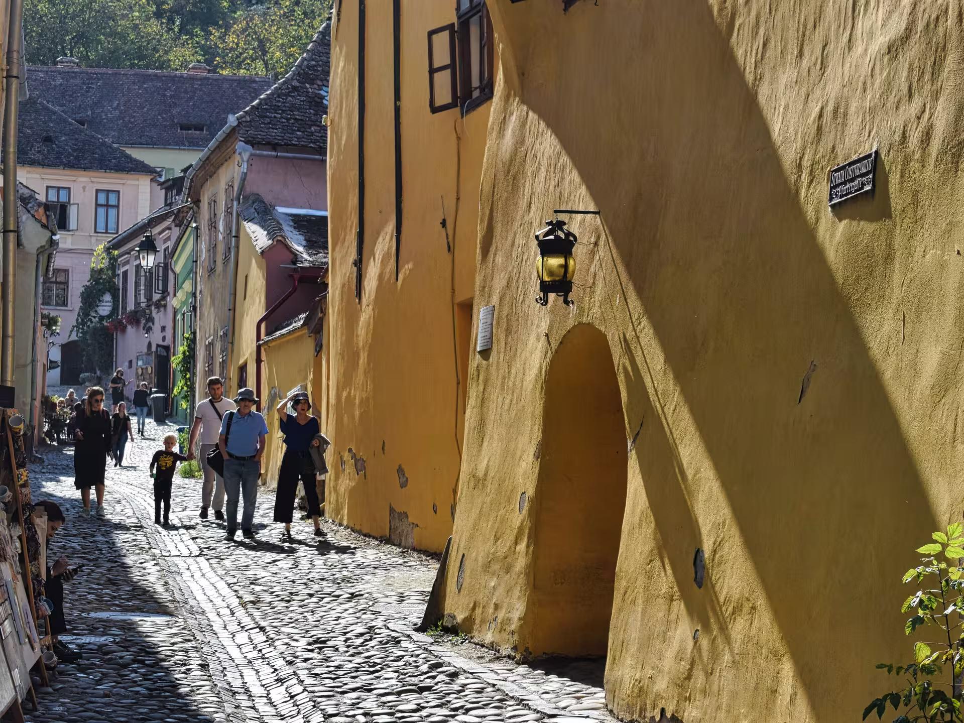 Tourists strolling along a sunny cobblestone street in Sighisoara medieval Saxon town Transylvania Romania