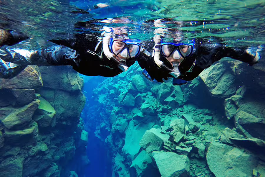 Snorkelers explore the crystal-clear waters of Silfra, Iceland, between tectonic plates in a drysuit snorkeling adventure.