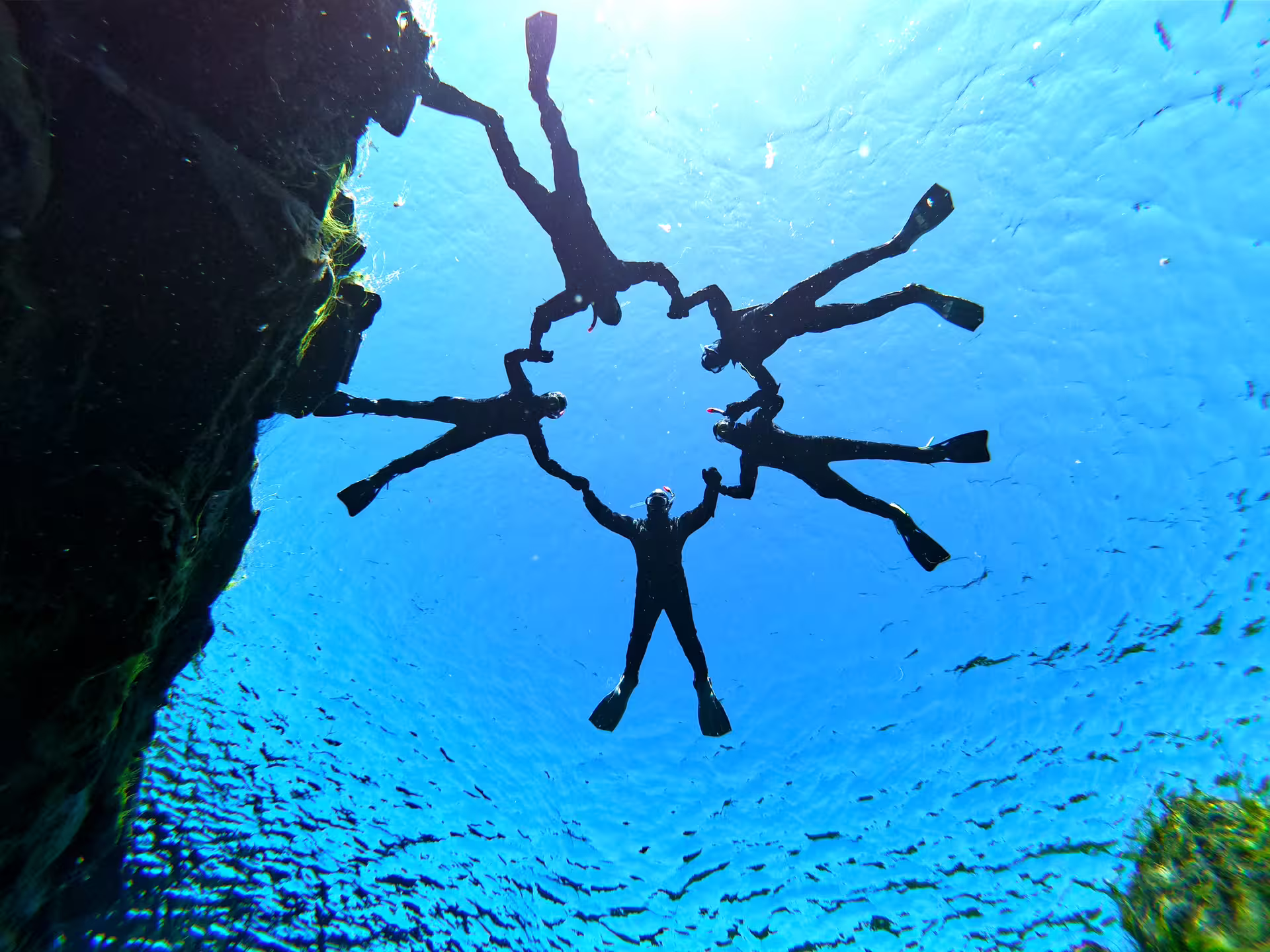 Snorkelers form a circle underwater in Silfra, Iceland, showcasing the clear blue waters and unique geological features.