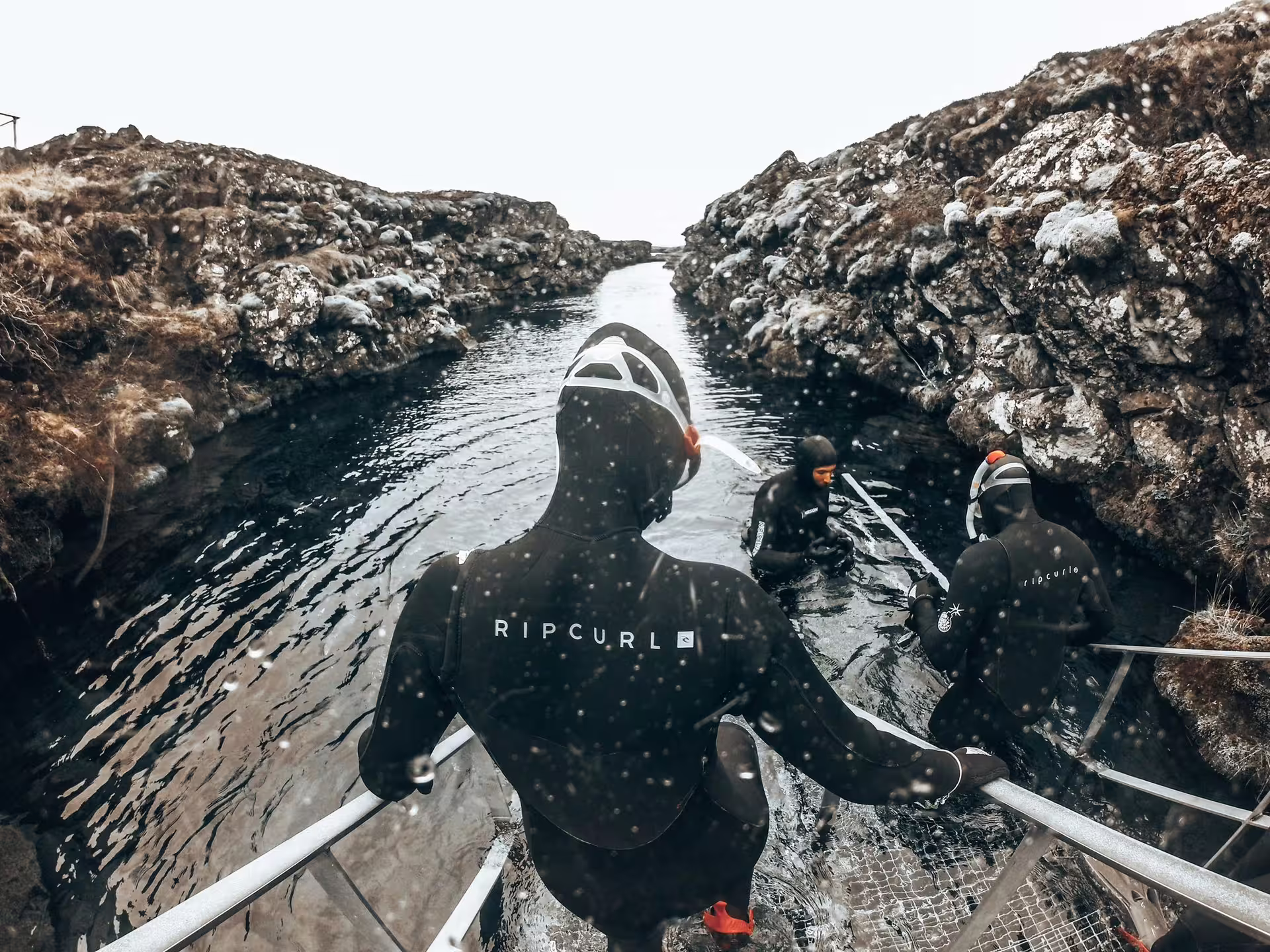 Snorkelers in wetsuits enter Silfra's crystal-clear waters in Iceland for an unforgettable underwater adventure.
