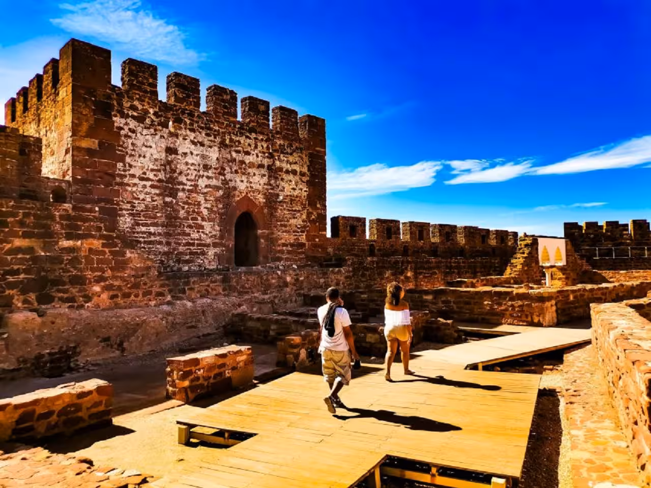Visitors walking along wooden walkways inside sunlit Silves Castle, exploring Algarve history on a Silves & Monchique tour