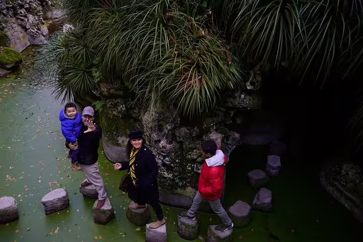 Family exploring lush gardens in Sintra on a private tour from Lisbon, stepping on stones over a serene green pond.