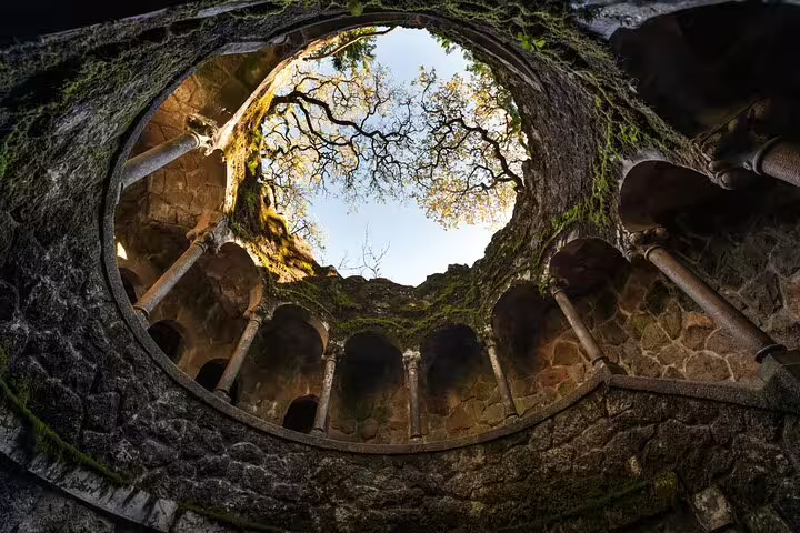 View of the mystical Initiation Well at Quinta da Regaleira in Sintra, showcasing its spiraling stone architecture and lush greenery.